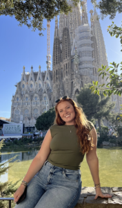 A woman in a green shirt smiling with a large building behind her. 